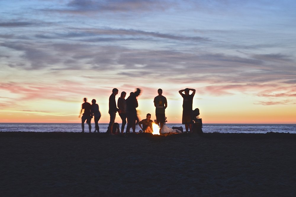 Unge mennesker hygger sig rundt om et bål på en strand