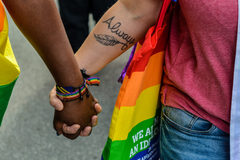 To hænder i forskellig hudfarve holder hånd under prideoptog