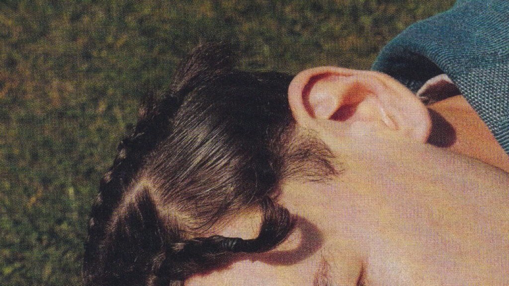 Close-up foto af person med mærke hår og fletninger som ligger på en græsplæne.