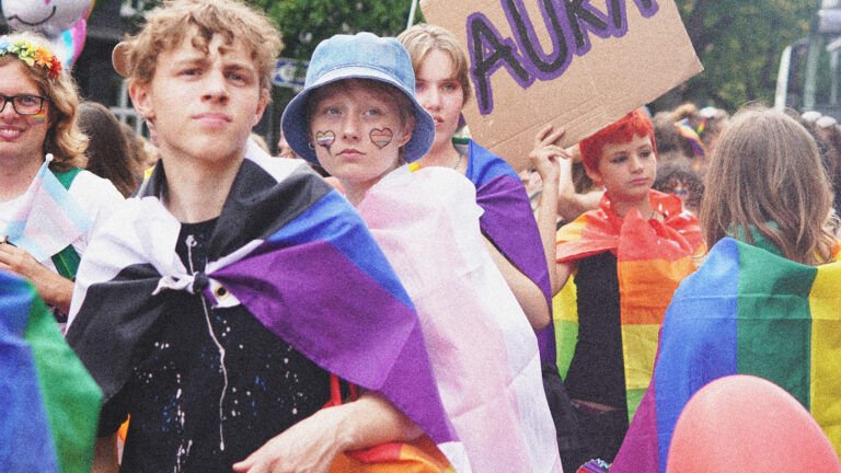 Unge LGBT+ personer ned regnbueflag om skuldrene som kapper og bannere i pride parade